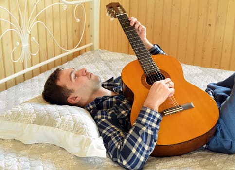 Young man playing guitar and laying on bed on weekend morning