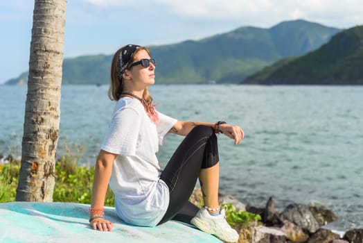 Young travel woman sitting with sunglasses and bandana on the shore of south china sea in vietnam