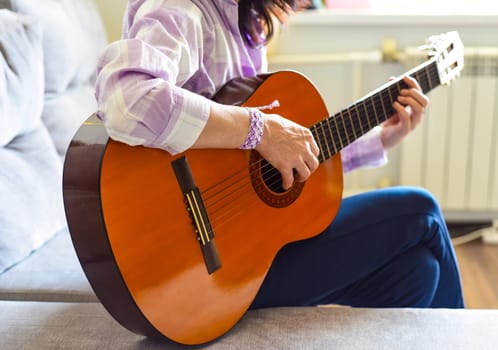 Russian woman playing guitar, sitting on a sofa at home.