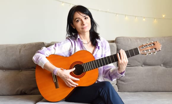 45 y.o. Russian woman playing guitar, sitting on a sofa at home.