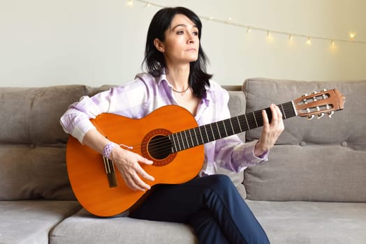 45 y.o. Russian woman playing guitar, sitting on a sofa at home.