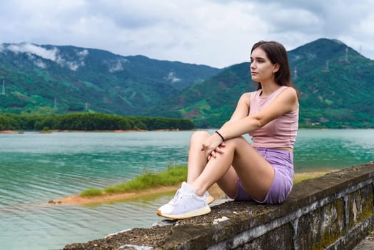 Young russian woman sitting with depressed and sad face against lake and mountains in Khanh Hoa Province, Vietnam