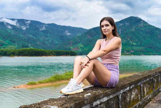 Young russian woman sitting with depressed and sad face against lake and mountains in Khanh Hoa Province, Vietnam