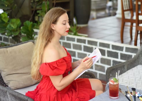 Beautiful blonde woman artist and illustrator thinking about idea of a drawing, sitting on a couch