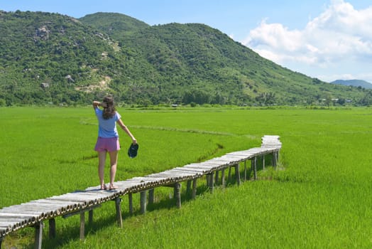 A young woman walking across wooden pier in a rice field