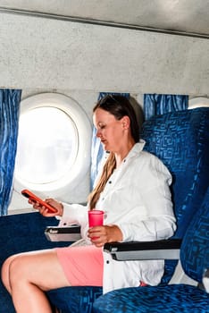 36 years old woman passenger scrolling phone, during a flight in the airplane cabin