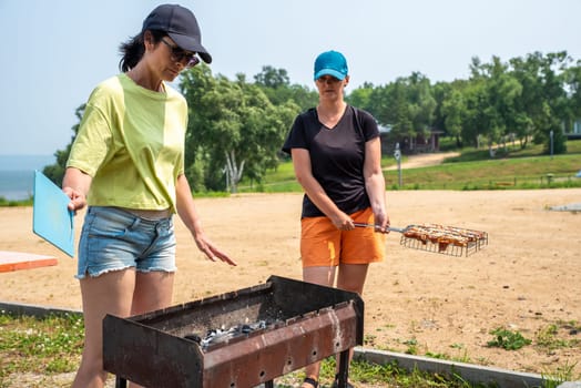 Two russian woman talking and cooking pork bbq on the beach of Japanese sea in the summer