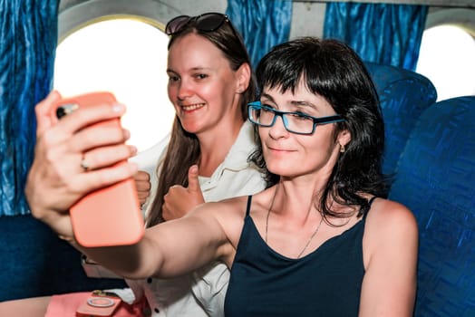 Two beautiful women passengers making a selfie, sitting in the airplane cabin