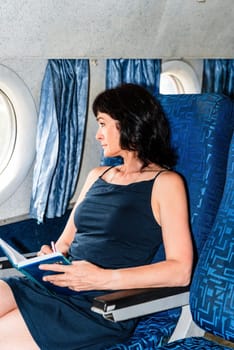 50 years old woman passenger writing in a notebook and thinking during a flight in the airplane cabin