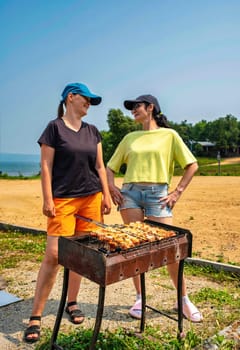 Two russian woman talking and cooking pork bbq on the beach of Japanese sea in the summer