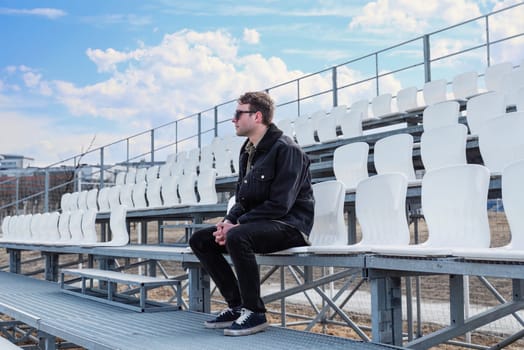 One young man sitting on empty football tribune on the street