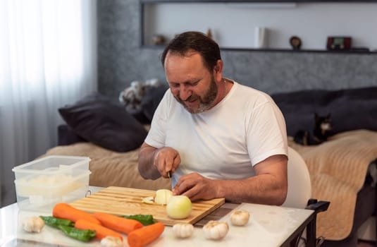 Mature man cooking pilaf, cutting vegetables in the kitchen at home