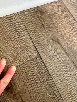 A close up view of vinyl plank flooring with visible gaps between the planks A hand is shown touching the surface highlighting the misalignment The wood grain texture of the planks gives a natural appearance despite the installation issue