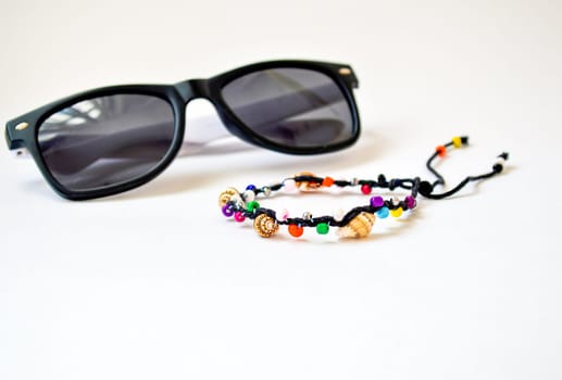 Handmade bracelet made of multi-colored beads and vietnamese seashells of the South China Sea, isolated on white background and blurred sunglasses