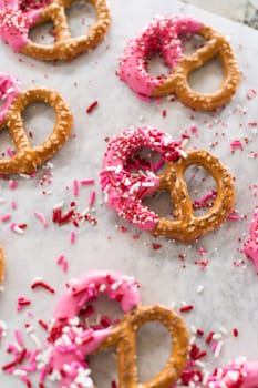 Freshly dipped and still glistening, these crunchy pretzels are lovingly adorned with pink chocolate and a scattering of colorful sprinkles, promising a feast for the senses.