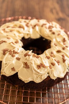 A gingerbread bundt cake being generously frosted with salted caramel frosting and topped with delightful gingerbread sprinkles.