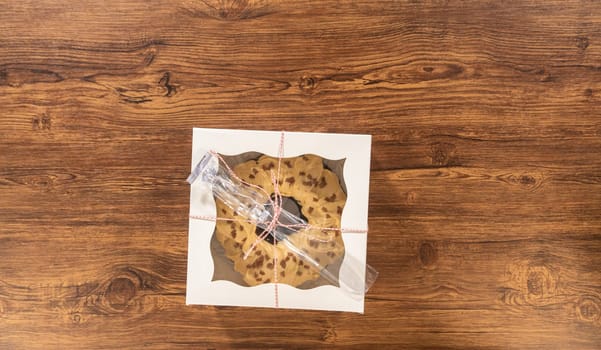 Flat lay. Carefully placing the gingerbread bundt cake, adorned with salted caramel frosting and gingerbread sprinkles, into a white paper bundt cake box with a clear window for gifting.