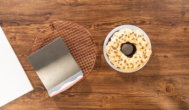 Flat lay. Carefully placing the gingerbread bundt cake, adorned with salted caramel frosting and gingerbread sprinkles, into a white paper bundt cake box with a clear window for gifting.