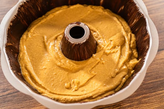 Pouring the gingerbread cake batter into the greased bundt cake pan, ready for a delightful caramel frosting.