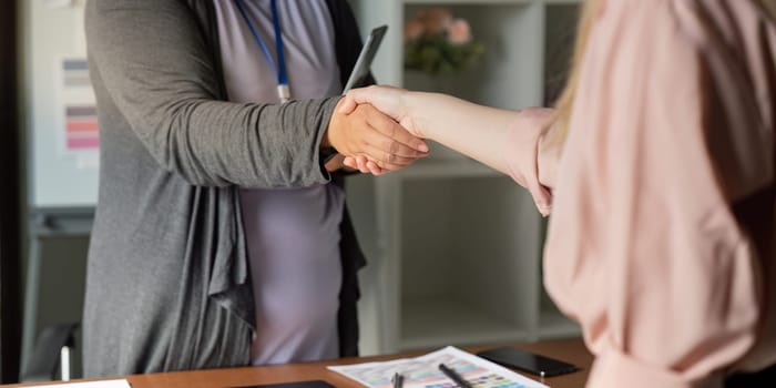 Graphic designers engaged in a handshake, symbolizing collaboration and partnership in a bright and inviting creative office space.