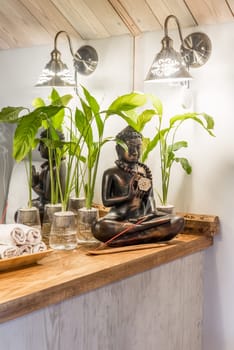 Spathiphyllum cochlearispathum commonly called peace lily growing in water in glass, with buddha