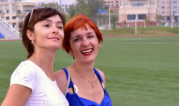 Two young russian sisters sincerely and naturally laughing with teeth in the summer evening on the football field