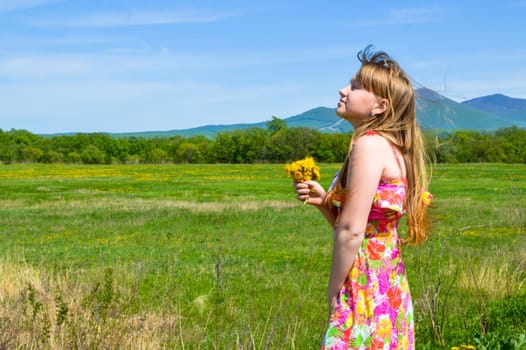 Blonde girl in dress holding bouquet of dandelion flowers with her head raised to the sun and her eyes closed.