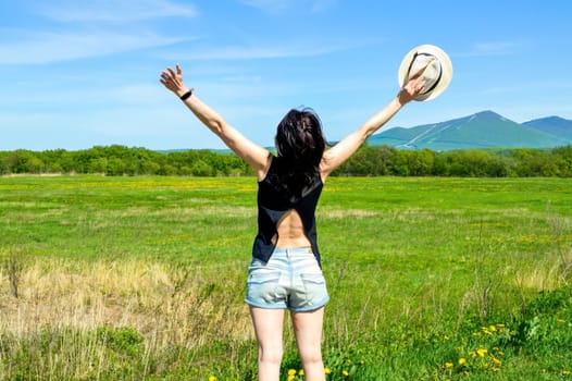 Brunette woman with hat embracing nature with open arms in countryside. copy space