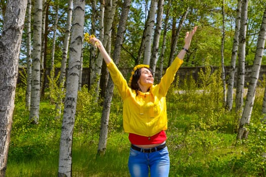 Brunette woman with bouquet of dandelions and wreath embracing nature with open arms in countryside. copy space