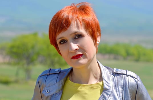 Portrait of Russian red-haired woman with short hair looking at the camera against the background of a field.