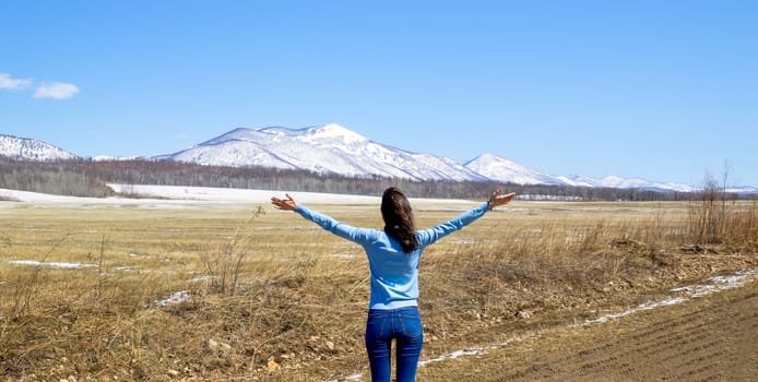 Slender brunette woman embracing  nature with open arms. The foot of the snowy mountains. concept of going out after quarantine. Russia, North Primorye.