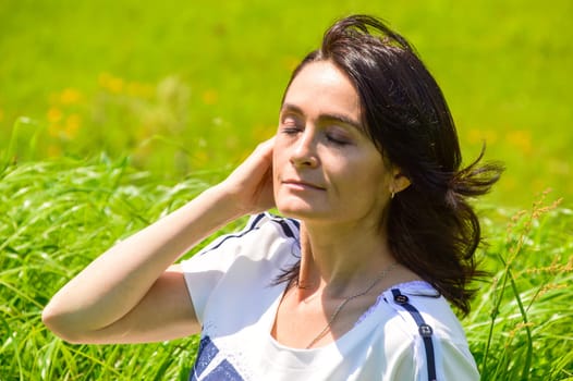 Portrait of 45 year old caucasian brunette woman with eyes closed on a green field. Enjoying the summer breath