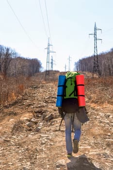 Young man with two colorful tourist rugs climbing up on an early spring day
