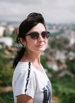 50 years old Russian brunette woman in sunglasses standing against vladivostok city view, portrait