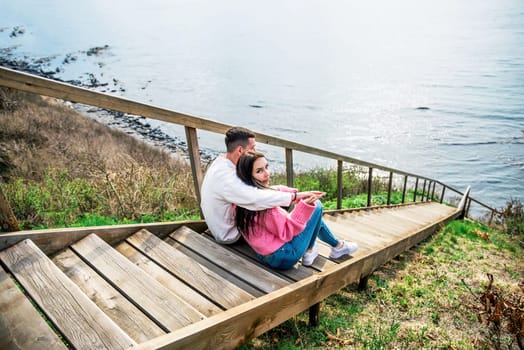 Young married couple sitting on the wooden long stairs and looking at Japanese sea