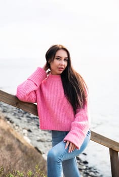 Young russian brunette woman in pink warm sweater standing on a wooden stairs