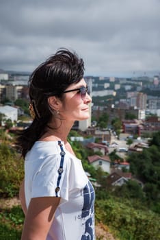 50 years old Russian brunette woman in sunglasses standing against vladivostok city view, portrait