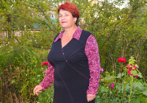 Elderly good-looking woman in dress smiling and standing near beautiful pink and red asters.