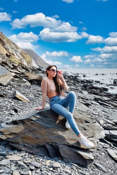 Young russian brunette woman in beige blouse sitting ont the stone near Japanese sea on a sunny day