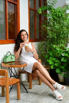 Portrait of 39 years old russian woman without make up sitting with glass of ice coffee in white dress