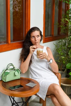 Portrait of 39 years old russian woman without make up sitting with glass of ice coffee in white dress.