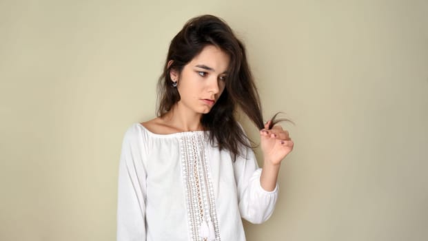 Portrait of young 25 y.o. brunette Russian woman with long hair. In white open shoulder top and looking into the camera on light gray background. Minimum makeup, natural hairstyle. copy space