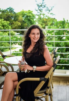 Portrait of 40 years old russian woman without make up sitting with glass of ice coffee in black dress