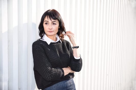 Young brunette woman 45 y.o. standing near a wooden white wall, looking to the side. Copy space