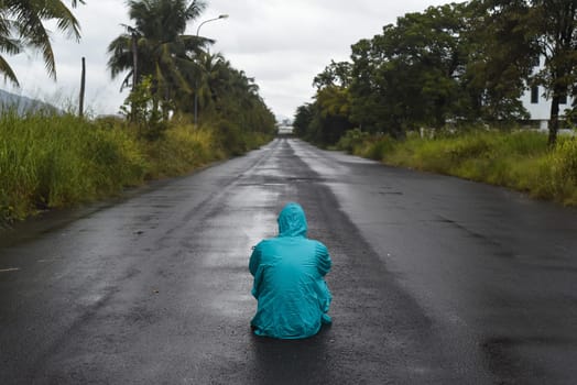 Depressive concept with lonely man in raincoat sitting on wet road under rain