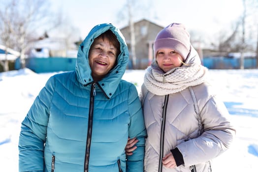 Portrait of Russian 12 y.o. girl and her grandmother looking at the camera on winter background.