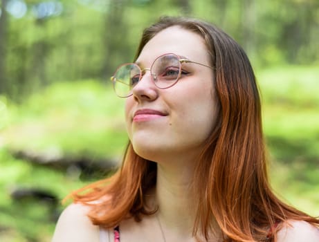 Teenage girl with dyed hair and glasses looking left against of green leaves
