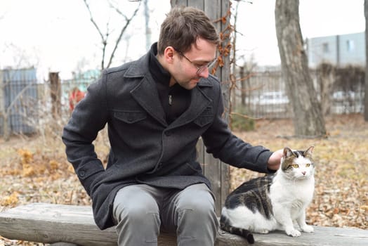 Young man sitting on a bench and petting a cat