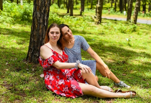 Mother hugging her teenage daughter with dyed hair and glasses against of green grass in the forest
