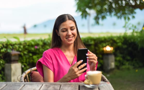 Beautiful brunette woman sitting by the table and taking photo of her cappuccino